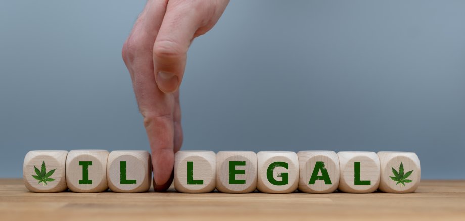 Symbol für die Legalisierung von Marihuana. Würfel bilden das Wort "ILLEGAL", während eine Hand die Buchstaben "IL" voneinander trennt, um das Wort in "LEGAL" zu ändern.