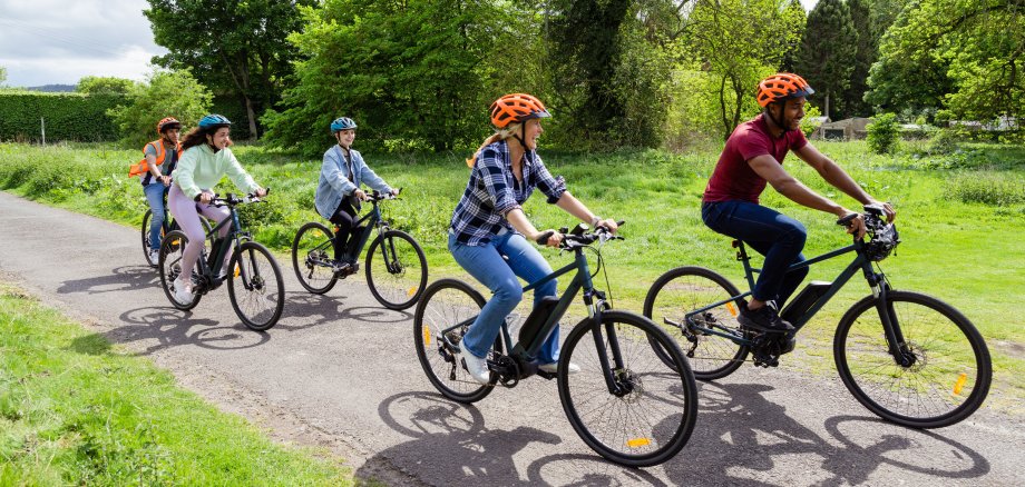 Aufnahme einer kleinen Gruppe von Radfahrern, die gemeinsam eine Fahrradtour in Hexham, Nordostengland, unternehmen. Sie tragen legere Kleidung und Fahrradhelme, lächeln und lachen, während sie radeln.